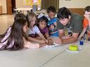 Children gathered at a table reaching into a paper plate with small objects.