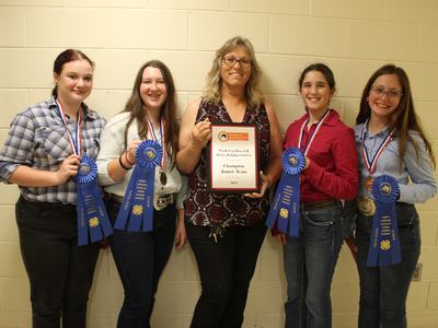 Five people standing holding a plaque reading "Champion Junior Team" and blue ribbons