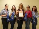 Five people standing holding a plaque reading "Champion Junior Team" and blue ribbons