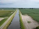 Straight canal between dirt road and crop fields in a rural landscape