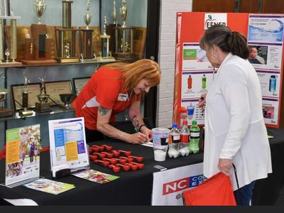 Staffer at health booth filling out a form while an attendee with a red bag watches