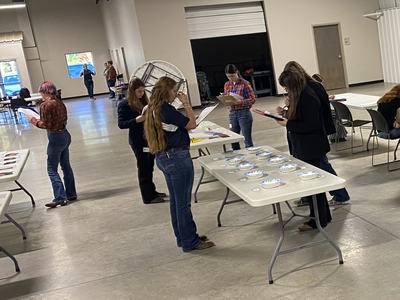 Several people standing at folding tables, inspecting papers and labeled paper plates