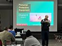 Instructor holding PPE in front of slide reading "Personal Protective Equipment, Chapter 8."