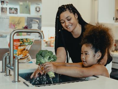 Mom and daughter washing broccoli in sink