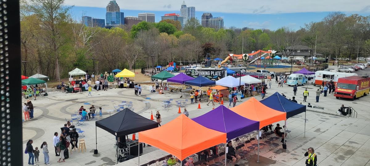 Community outdoor festival with colorful vendor tents and "SPINNING PLATE" food truck