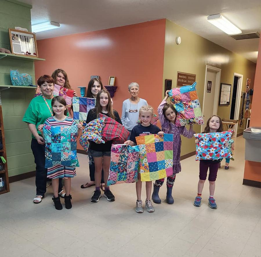 Women and girls in hallway holding colorful patchwork quilts and pillows