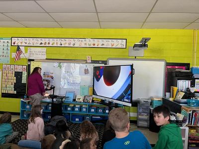 Teacher at front of classroom showing students a magnified image on a large screen
