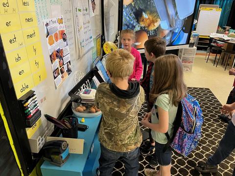 Elementary students gathered around a classroom egg incubator observing eggs.