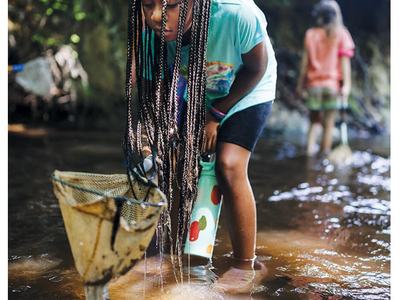 Girl with long braids wading in a stream, scooping water with a net