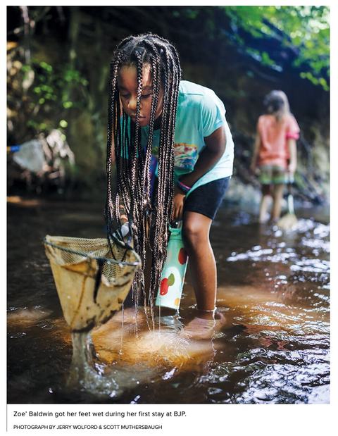 Girl with long braids wading in a stream, scooping water with a net