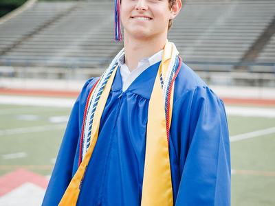 A young man standing on a football field in a graduation cap and gown.