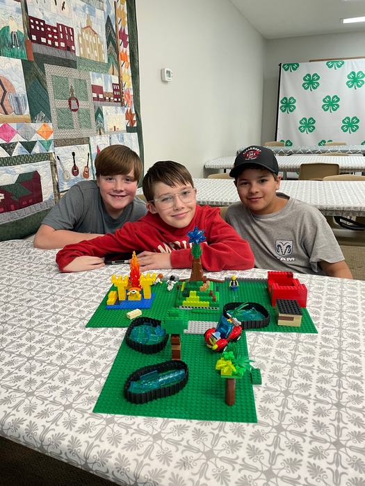 Three children at a table displaying a LEGO landscape with 4‑H backdrop