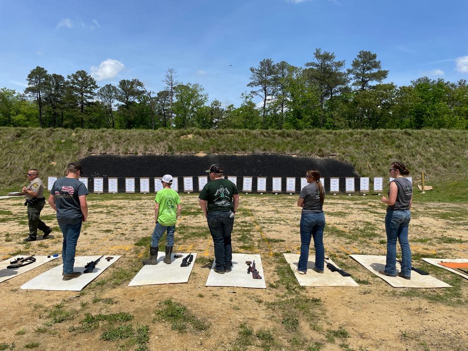 Several people standing on firing mats at an outdoor shooting range facing paper targets