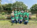 Group of volunteers wearing green shirts posing in a raised-bed community garden