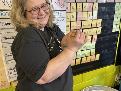 Woman holding a small yellow chick in a classroom, metal tub with chicks and waterer nearby
