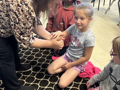 Adult bending over to hold a seated girl's hands while other children sit nearby
