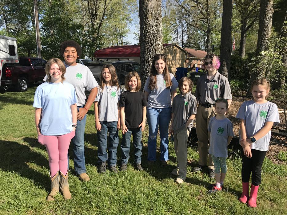 Group of children and teens wearing 4‑H shirts standing on grass by trees