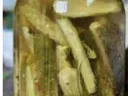Glass jar of pickled okra spears in brine with visible mustard seeds