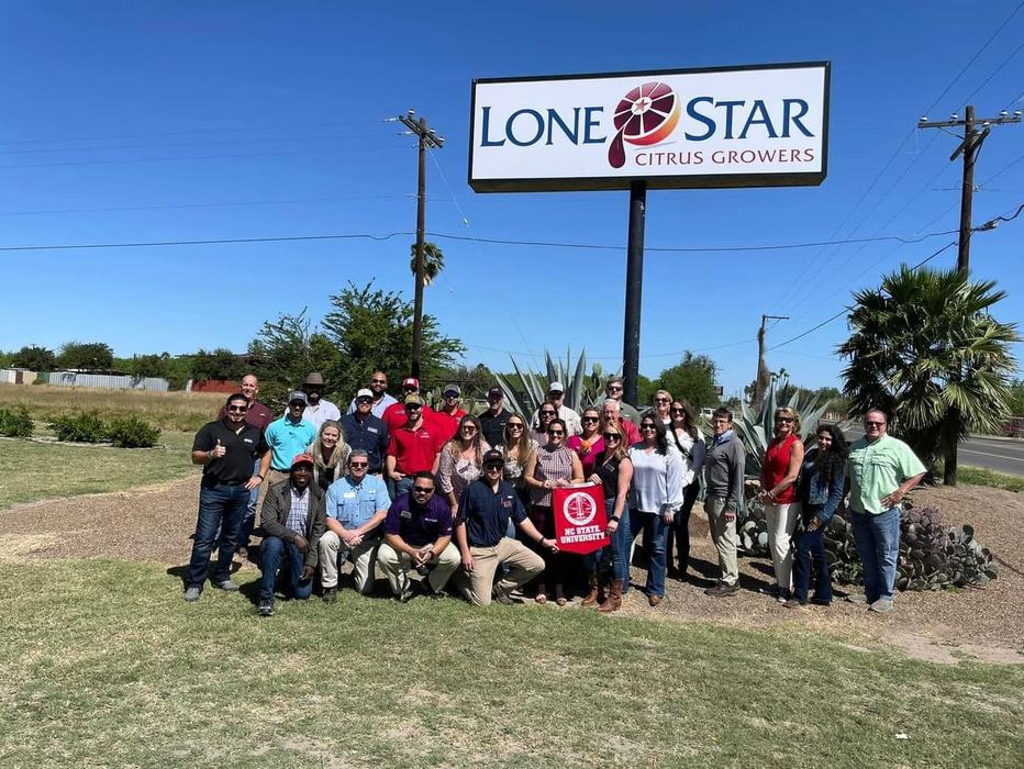 A group poses with an NC State University banner in front of a sign reading Lone Star Citrus Growers.