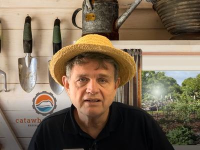 Person wearing straw hat in a gardening shed with hanging trowels and "catawba" logo