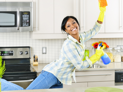 Person leaping in kitchen while holding a sponge and cleaning products.
