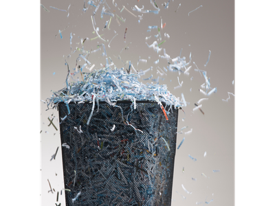 Mesh wastebasket overflowing with shredded paper, strips scattering and falling around it