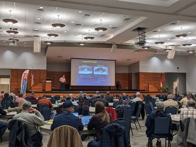 Presenter on stage giving a slideshow to a seated audience in a conference hall