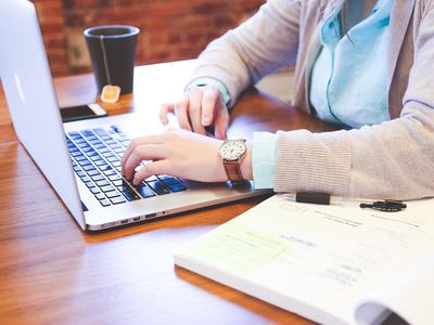Person sitting in front of an open laptop with a cup of coffee and an open notebook