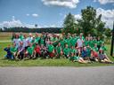 Large group of children and teens wearing green shirts posing outdoors on grass