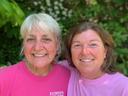 Two women in pink "RAYMOND'S GARDEN CENTER" shirts standing side-by-side, leafy background