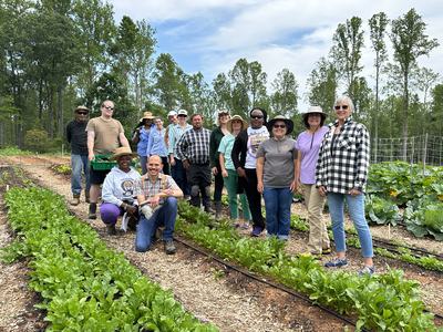 Group of people standing in a vegetable garden among rows of leafy greens
