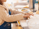 Child wearing apron rolling dough with a rolling pin on a floured counter