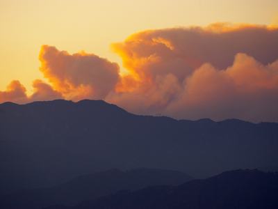 Sunset-lit smoke plumes rising behind dark mountain ridges