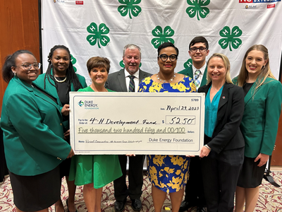 A group stands together with a check in front of a 4-H Backdrop.