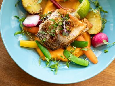 Pan-seared fish fillet on orange puree with potatoes, snap peas, radishes, lime wedge