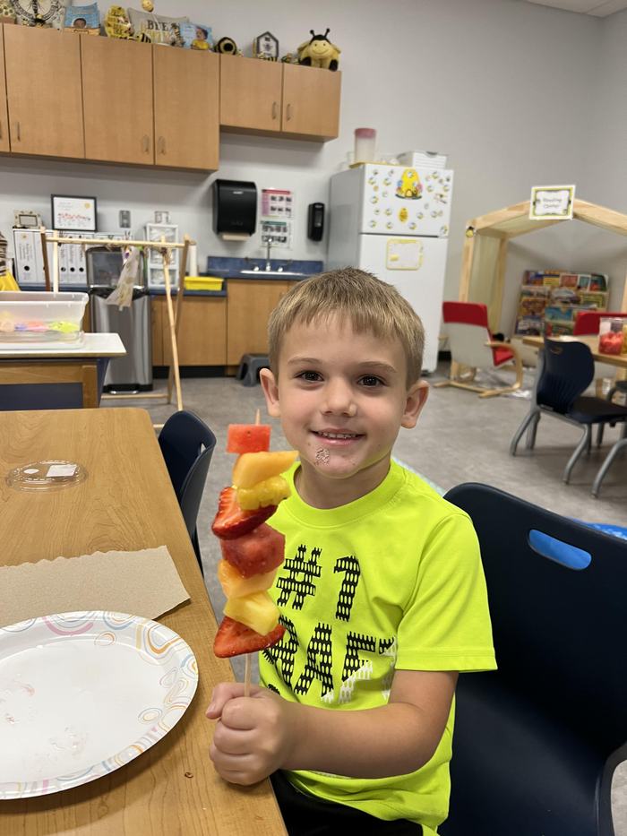 A child shows the fruit skewer he made.