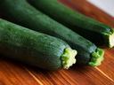 Three green zucchinis lying on a wooden cutting board.