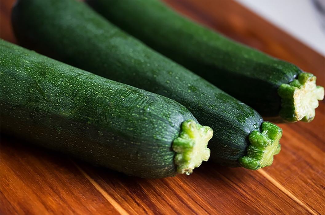 Three green zucchinis lying on a wooden cutting board.