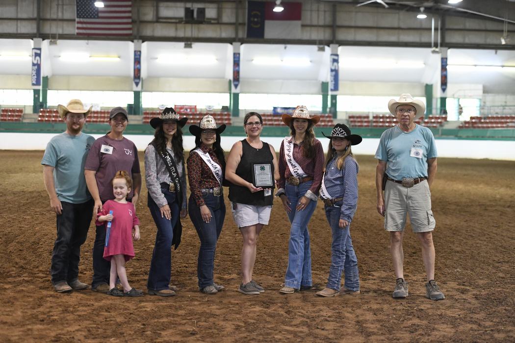 Group of people in western wear posing in indoor arena, center woman holding a plaque