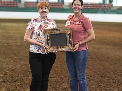 Two women standing in an arena holding a plaque labeled "KAREN JONES"
