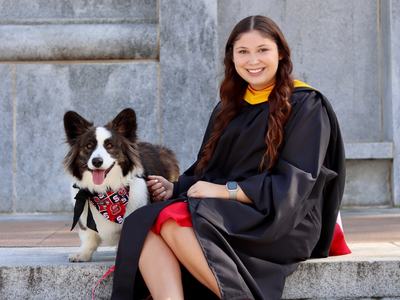 A girl in graduation gown poses with dog.