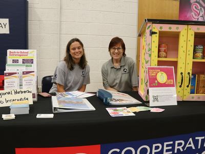 Two AmeriCorps staff seated at a table with food security materials and sign "Regional Partnership Food Insecurity"