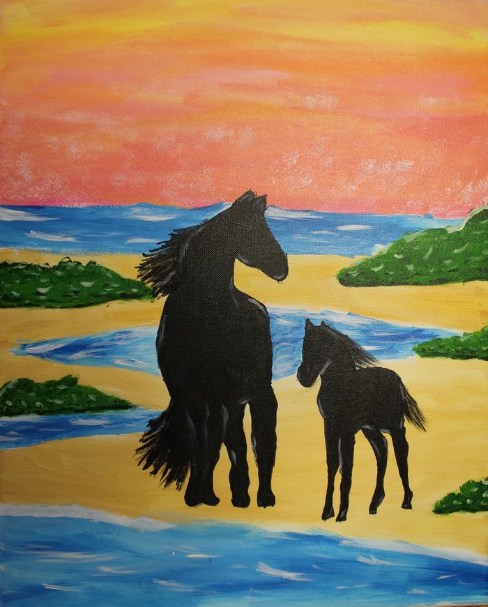 Adult horse and foal silhouettes standing on a sandy shoreline with ocean and sunset sky