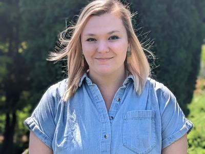 Woman standing outdoors in front of trees wearing a light denim shirt