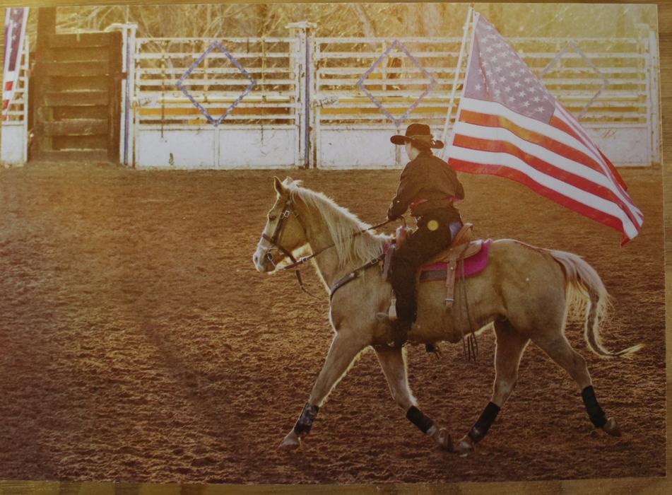 Cowboy-hatted rider carrying American flag while trotting palomino horse in arena