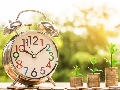 Analog alarm clock beside three coin stacks with seedlings growing larger left to right