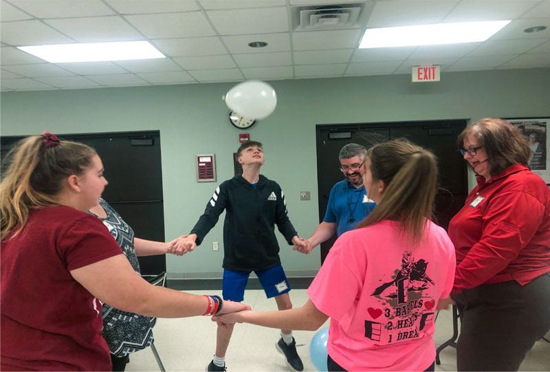 group of youth playing a game, bouncing a balloon to each other with their head.