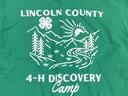 Green shirt: "LINCOLN COUNTY" with 4-H clover, mountains and river, "4-H DISCOVERY Camp"