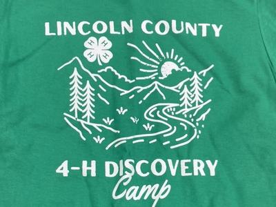 Green shirt: "LINCOLN COUNTY" with 4-H clover, mountains and river, "4-H DISCOVERY Camp"