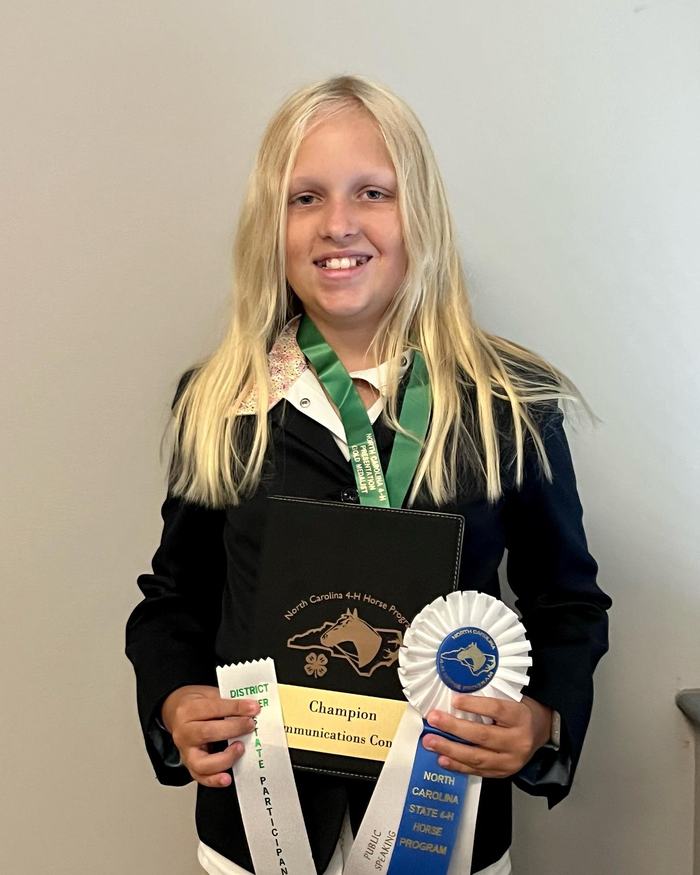 Youth with medal holding plaque reading "Champion Communications" and "NC 4‑H Horse" ribbon